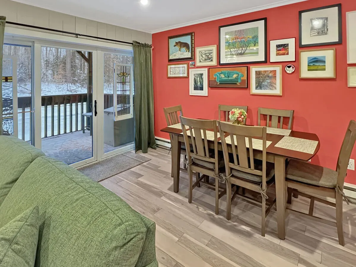 A cozy dining area featuring a stylish dining table, a vibrant art wall, and a plush green couch, with a sunlit sliding door suggesting easy access to outdoor spaces. The scene radiates warmth and comfort, ideal for gatherings, meals, or unwinding after a day of adventure.