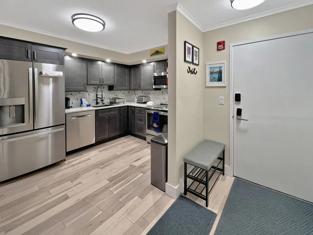 A welcoming, modern kitchen with sleek appliances, wooden flooring, and family-friendly touches like an entryway bench and framed pictures. The atmosphere exudes warmth and comfort, ideal for gathering and sharing meals after a day of adventure.