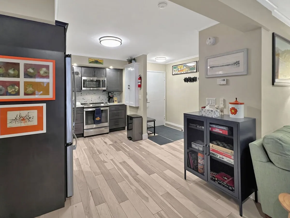 A warm, inviting open-concept living and kitchen area featuring modern appliances, abundant cabinetry, and tasteful wall art. The space is set up for group cooking and entertaining, with plenty of room for guests to gather, share meals, or relax together by the kitchen.