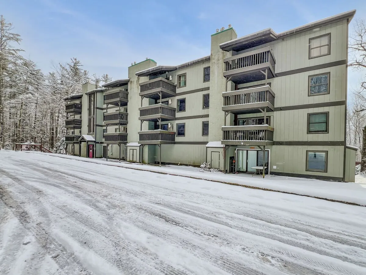 This image displays the exterior of the apartment building surrounded by snow, with balconies and a tranquil, wintry landscape. The view highlights the connection to outdoor activities and the serene mountain setting, reflecting the property's proximity to winter attractions and opportunities for family fun in nature.