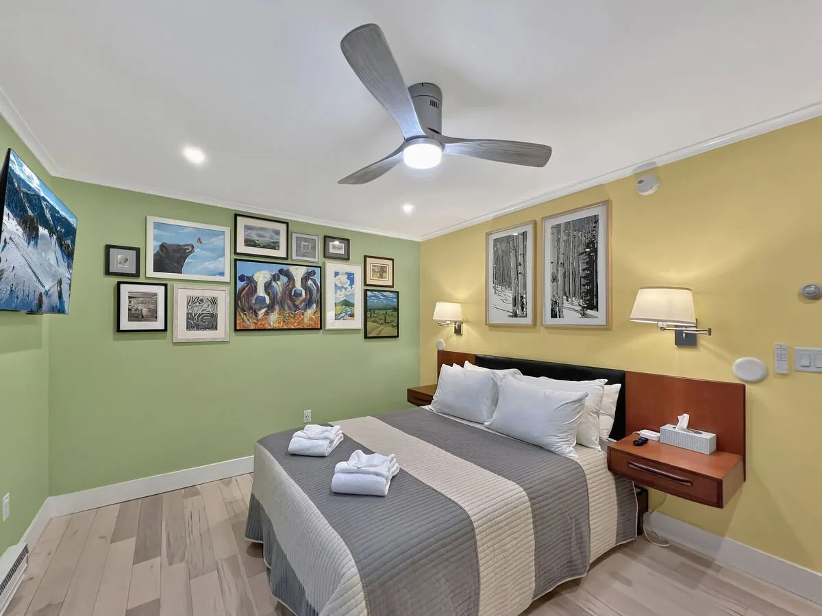 A cozy bedroom scene with a neatly made bed adorned with fresh towels, wall art, and a television. The atmosphere is inviting, suggesting relaxation and comfort after group adventures or a shared movie night in.