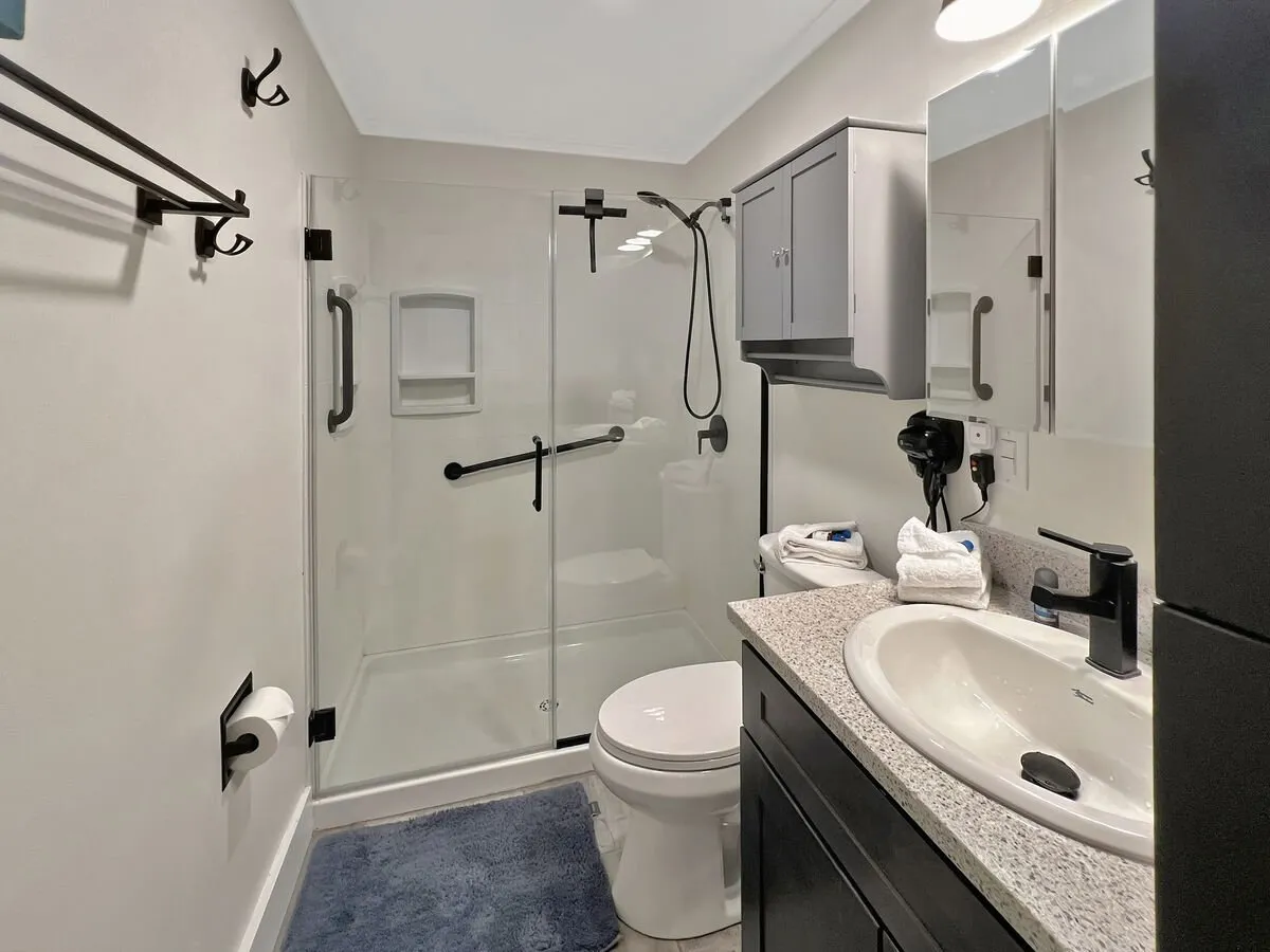 A bright, fresh bathroom with a glass-enclosed shower area, modern sink, toilet, and a large mirror above the vanity. The space is clean, inviting, and well-maintained, ideal for refreshing and preparing for the day.
