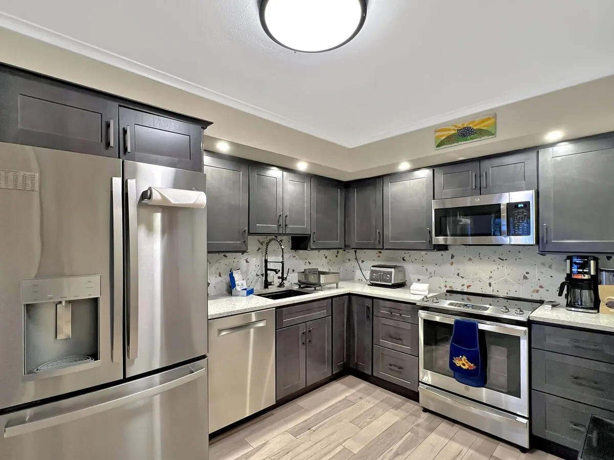 The image showcases a modern kitchen with stainless steel appliances, granite countertops, and contemporary cabinetry. Colorful artwork adds warmth, and the setup is clearly designed for sociable meal prep and gatherings, highlighting both functionality and style.