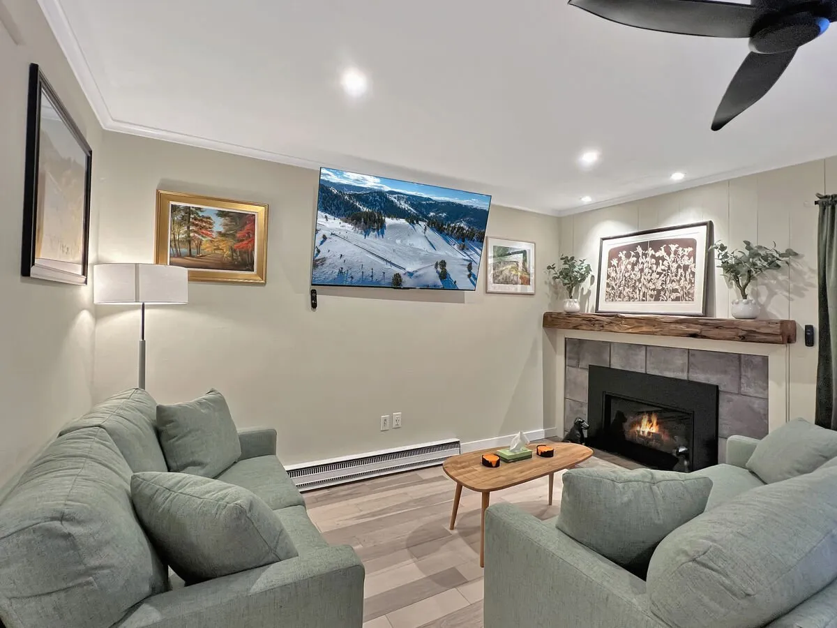 This image centers on the heart of the living area, showing a plush sofa oriented toward a warm gas fireplace and a large TV. The scene includes a coffee table and tasteful artwork, creating an inviting space for relaxation, movie nights, or gathering after outdoor adventures.